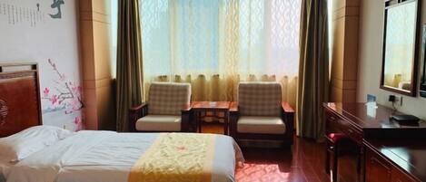 A hotel room with a bed, two chairs, a small table, a desk, and a mirror.