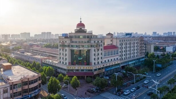 Un edificio de varios pisos con una cúpula roja destacada, rodeado de árboles y una calle concurrida.