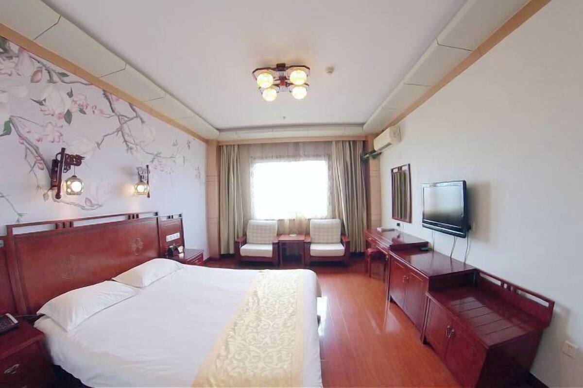 A hotel room with a large bed, a desk with a chair, a television, and a window with curtains.