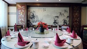 Una mesa de comedor redonda con servilletas rosas, platos blancos y un jarrón de flores rojas.