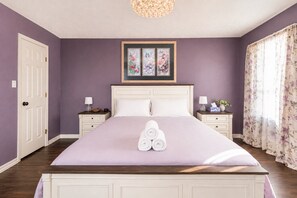 Ein Schlafzimmer mit einem großen Bett, zwei Nachttischen, einer Tür und einem gerahmten Kunstwerk über dem Bett.