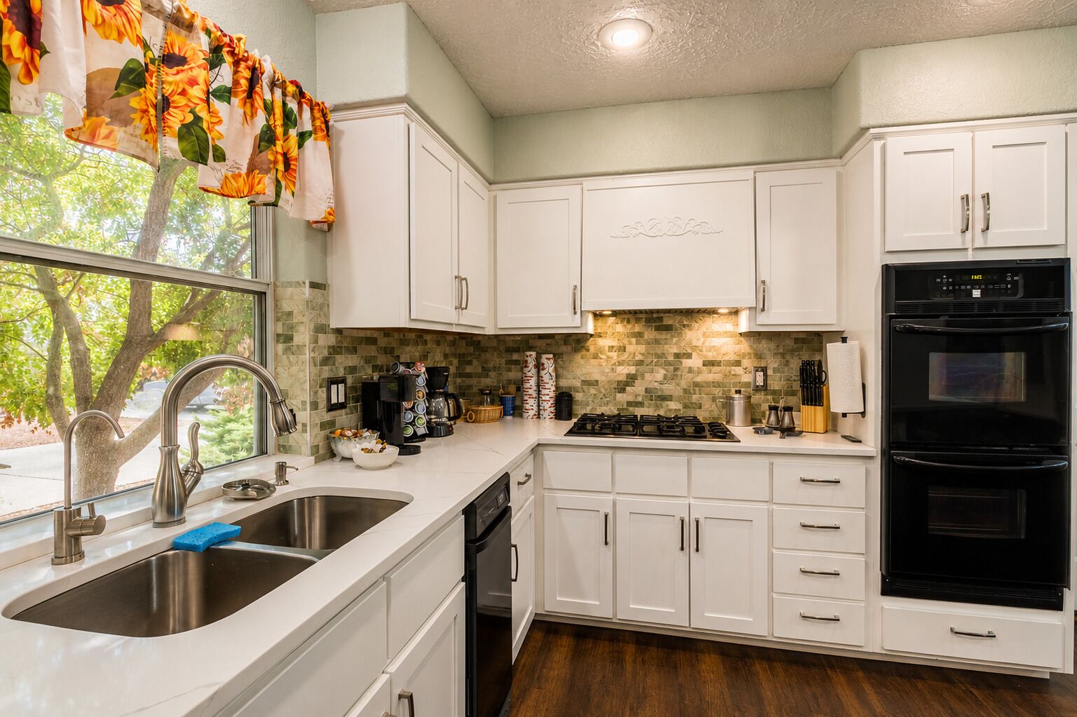 A modern kitchen with white cabinets, a stainless steel sink, a gas stove, and a black oven.