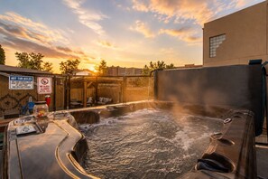 Un bain à remous dont la vapeur s'élève, entouré d'une clôture et de chaises longues, avec un coucher de soleil en arrière-plan.