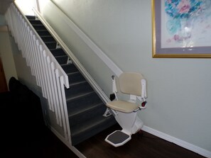 Una escalera con barandilla, un sillón con reposapiés y un cuadro en la pared.