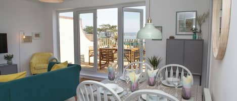 A living room with a sofa, dining table, chairs, and a view through a glass door to an outdoor patio.