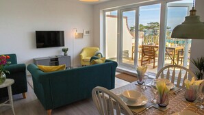A living room with a sofa, TV, and a dining area with a table set for two. - Gweld y Mor, Saundersfoot (Saundersfoot)