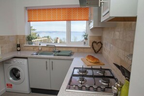 A kitchen with a washing machine, a stove, a sink, and a window with a view. - Gweld y Mor, Saundersfoot (Saundersfoot)