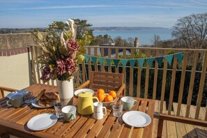 A wooden table set with breakfast items, a vase with flowers, and a view of the sea. - Gweld y Mor, Saundersfoot (Saundersfoot)