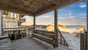 A wooden deck with benches and tables, overlooking a beach with dunes and the ocean. - 'Loophole' | Oceanfront | Historic Cottage (Nags Head)