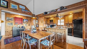 A spacious kitchen with wooden cabinetry, a dining area with a wooden table and chairs, and a refrigerator. - 'Loophole' | Oceanfront | Historic Cottage (Nags Head)