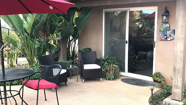 An outdoor patio area with a red umbrella, black wicker chairs, and a glass door leading to a covered space.