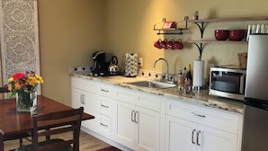 A modern kitchen with white cabinets, a stainless steel refrigerator, a microwave, and a kettle on the countertop.