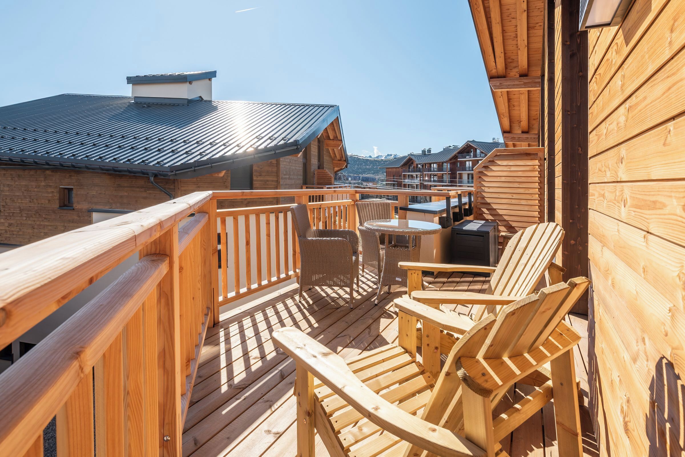 Eine Holzterrasse mit Gartenmöbeln, Blick auf andere Gebäude und einem klaren Himmel.