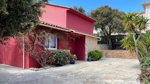 A red building with a stone-paved courtyard, surrounded by potted plants and trees.