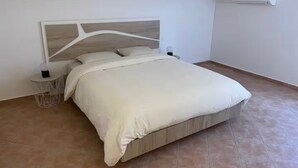 A bedroom with a bed, a bedside table, a wall-mounted air conditioner, and a wooden ceiling beam.