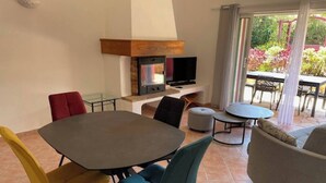 A modern living room with a round dining table, colorful chairs, a grey sofa, and a TV mounted on a wooden wall.