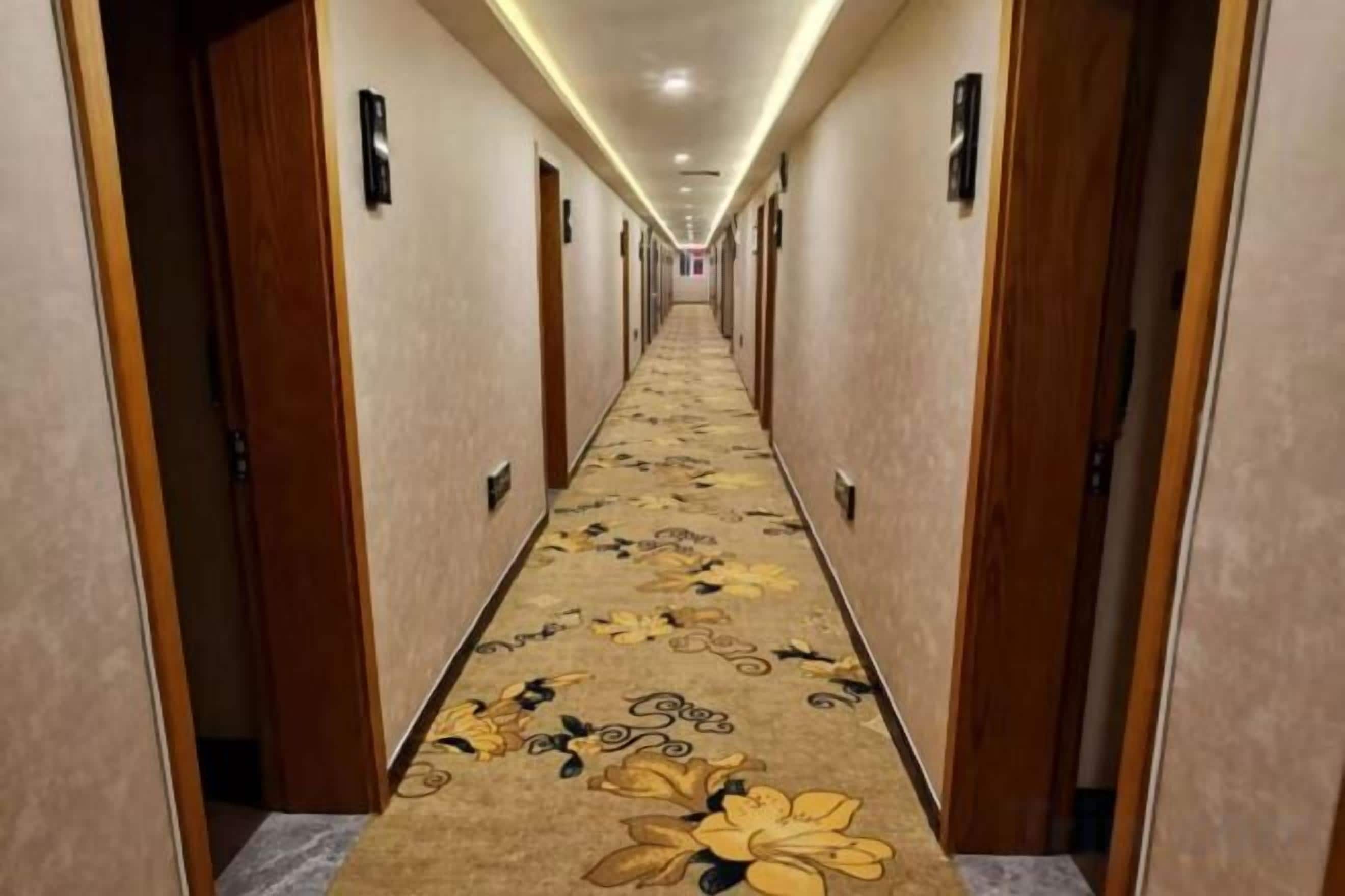 A hotel hallway with carpeted floors, doors on both sides, and a lighted ceiling.