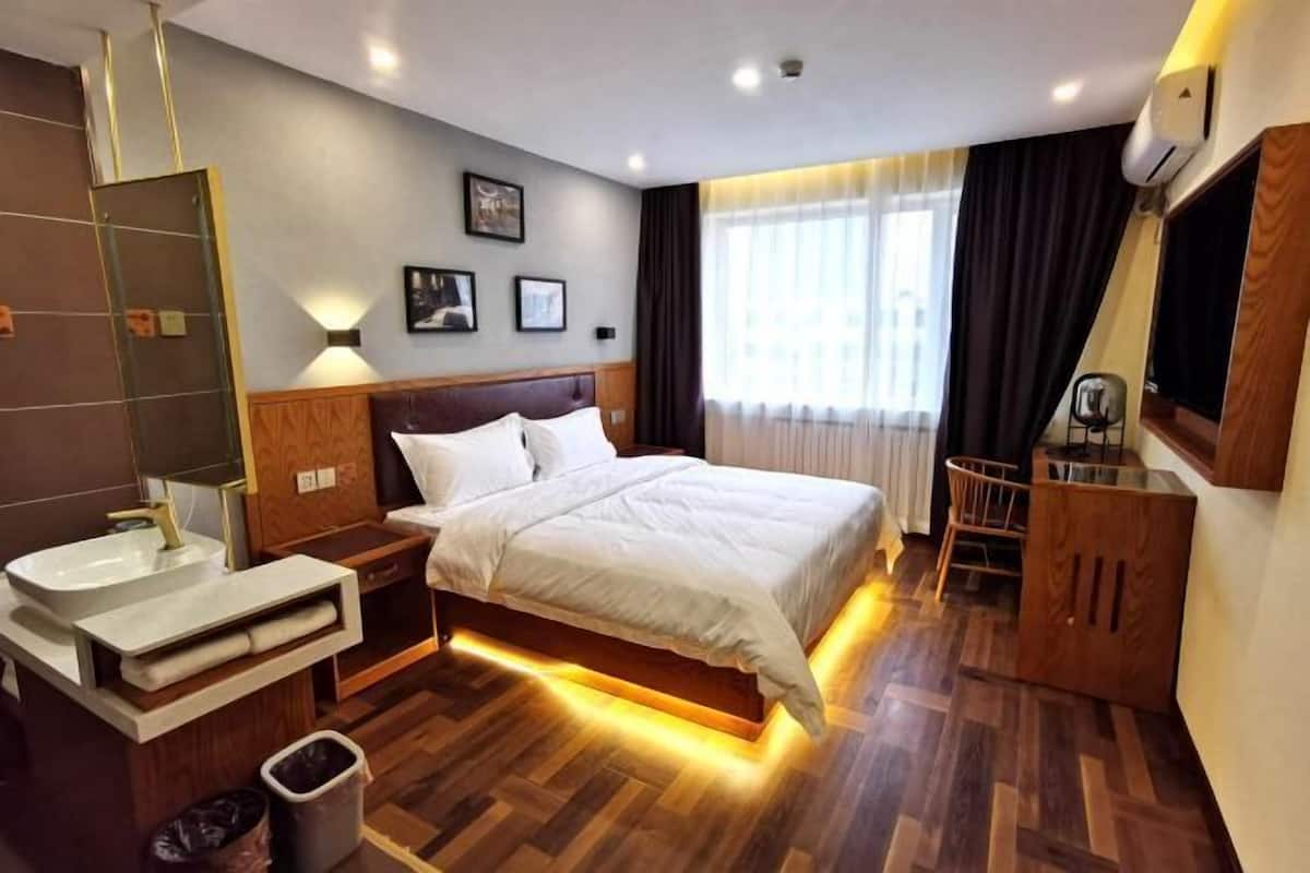 A hotel room with a bed, bedside table, vanity with sink, and a TV.