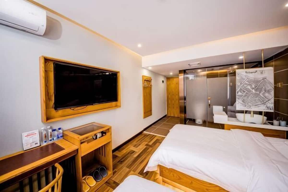 A hotel room with a TV, wooden furniture, a desk with toiletries, a bed, and a bathroom with a mirror and towel rack.