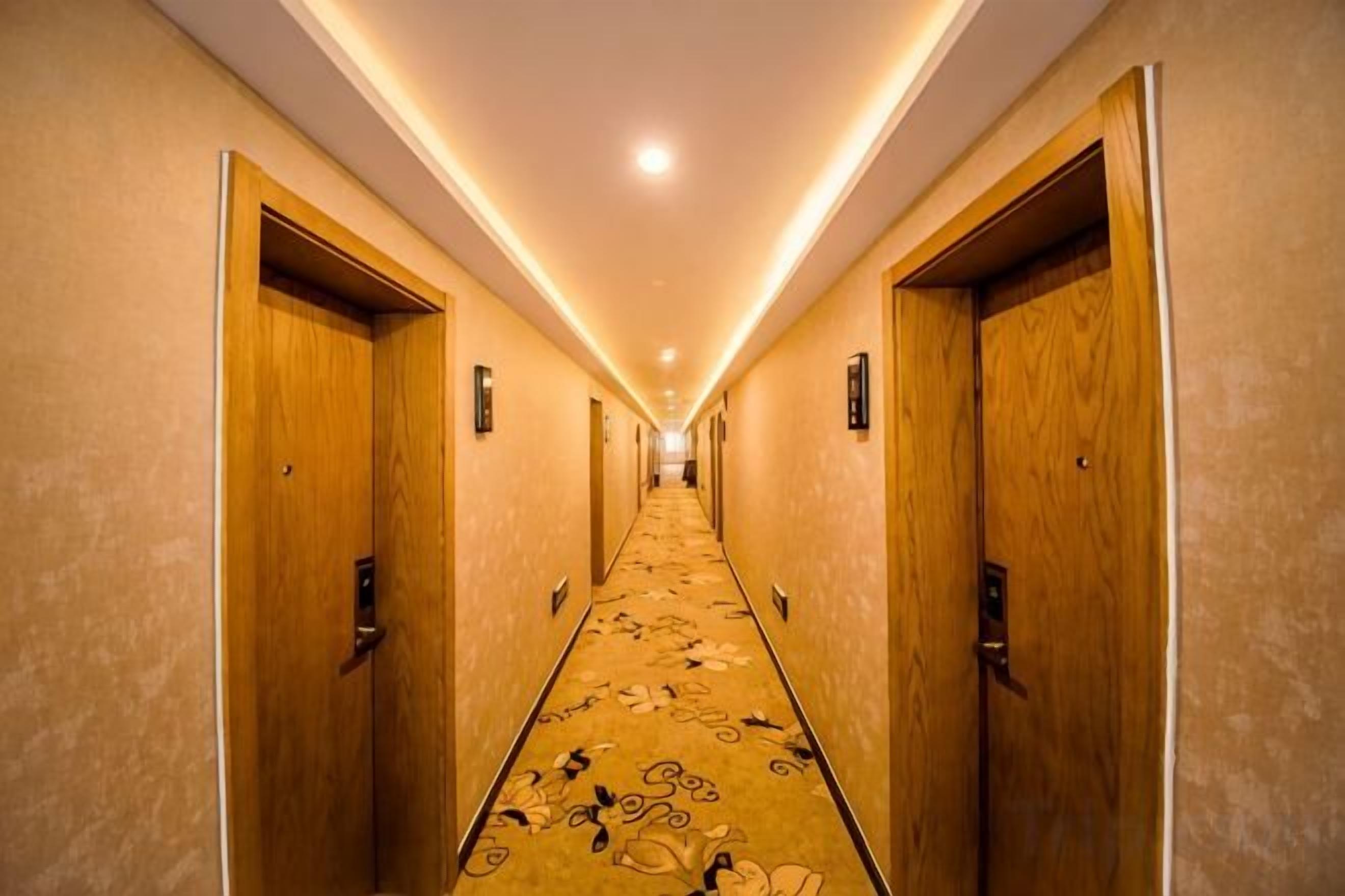 Un pasillo de hotel con puertas de madera, suelo alfombrado e iluminación empotrada.