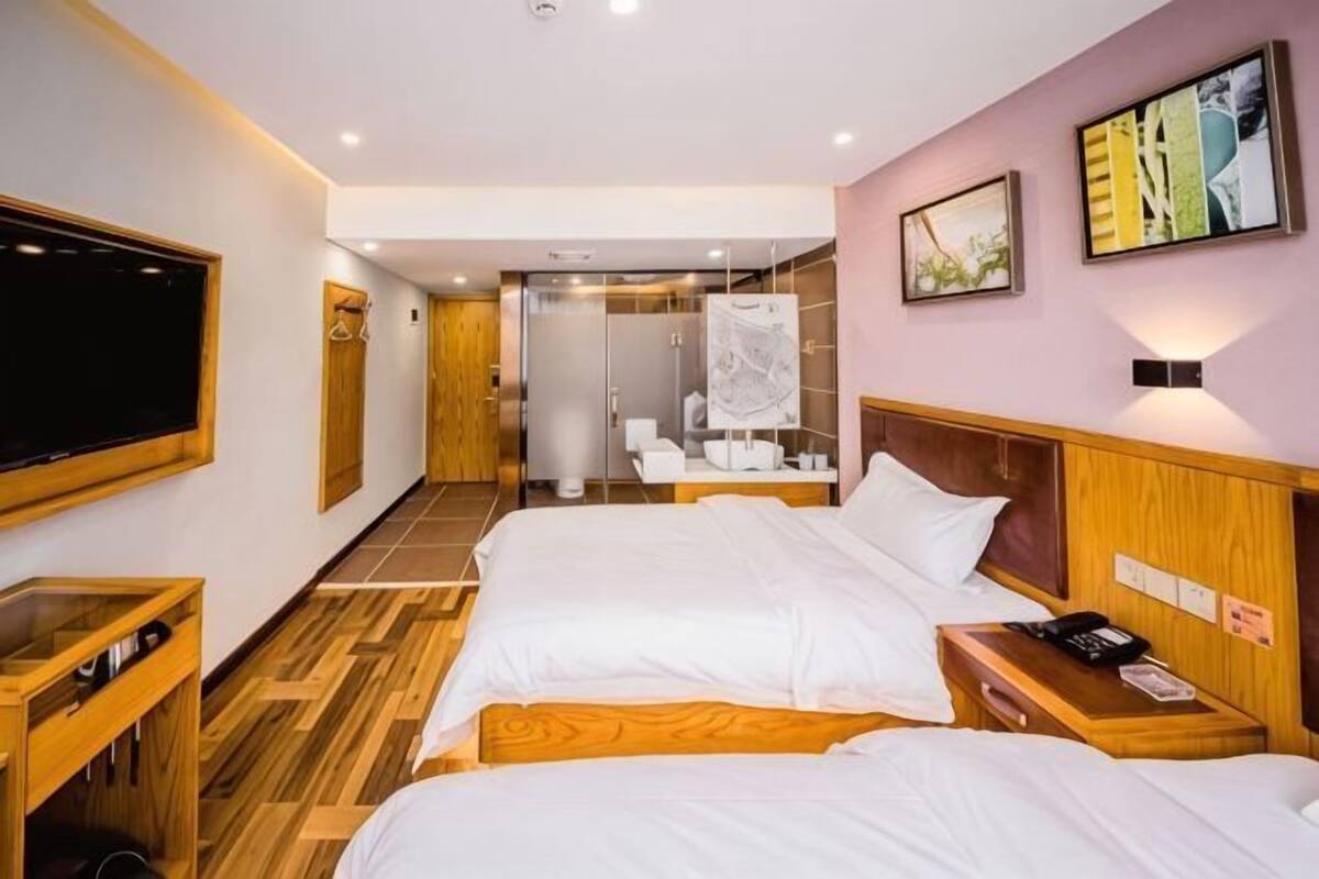 A hotel room with two beds, a TV, a wooden cabinet, and a shower area.