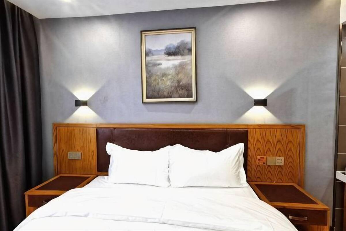 A hotel room with a bed, two bedside tables, a nightstand, a wall-mounted lamp, and a framed picture.