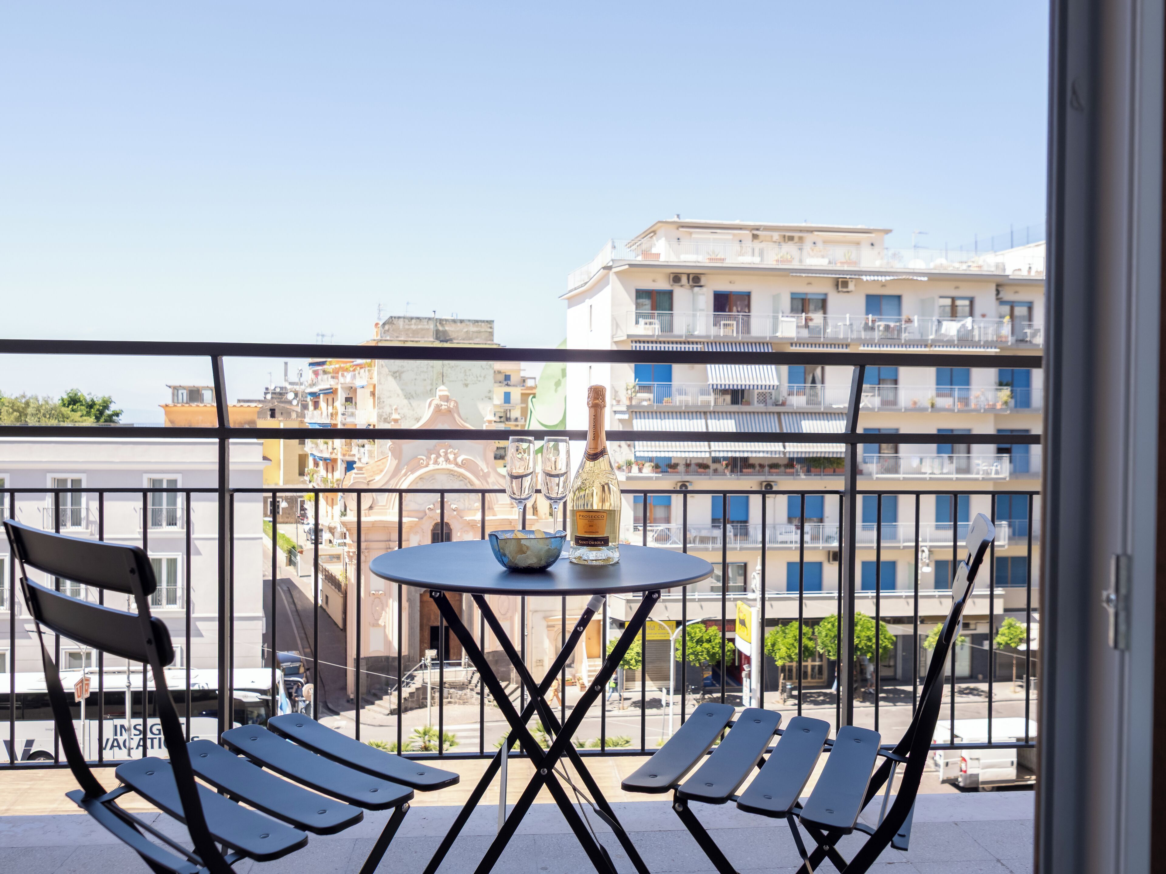 Un balcone con due sedie nere, un piccolo tavolo rotondo e una bottiglia di champagne.