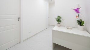 Un pasillo con una puerta blanca, una consola blanca con dos plantas en macetas, y una pared blanca.