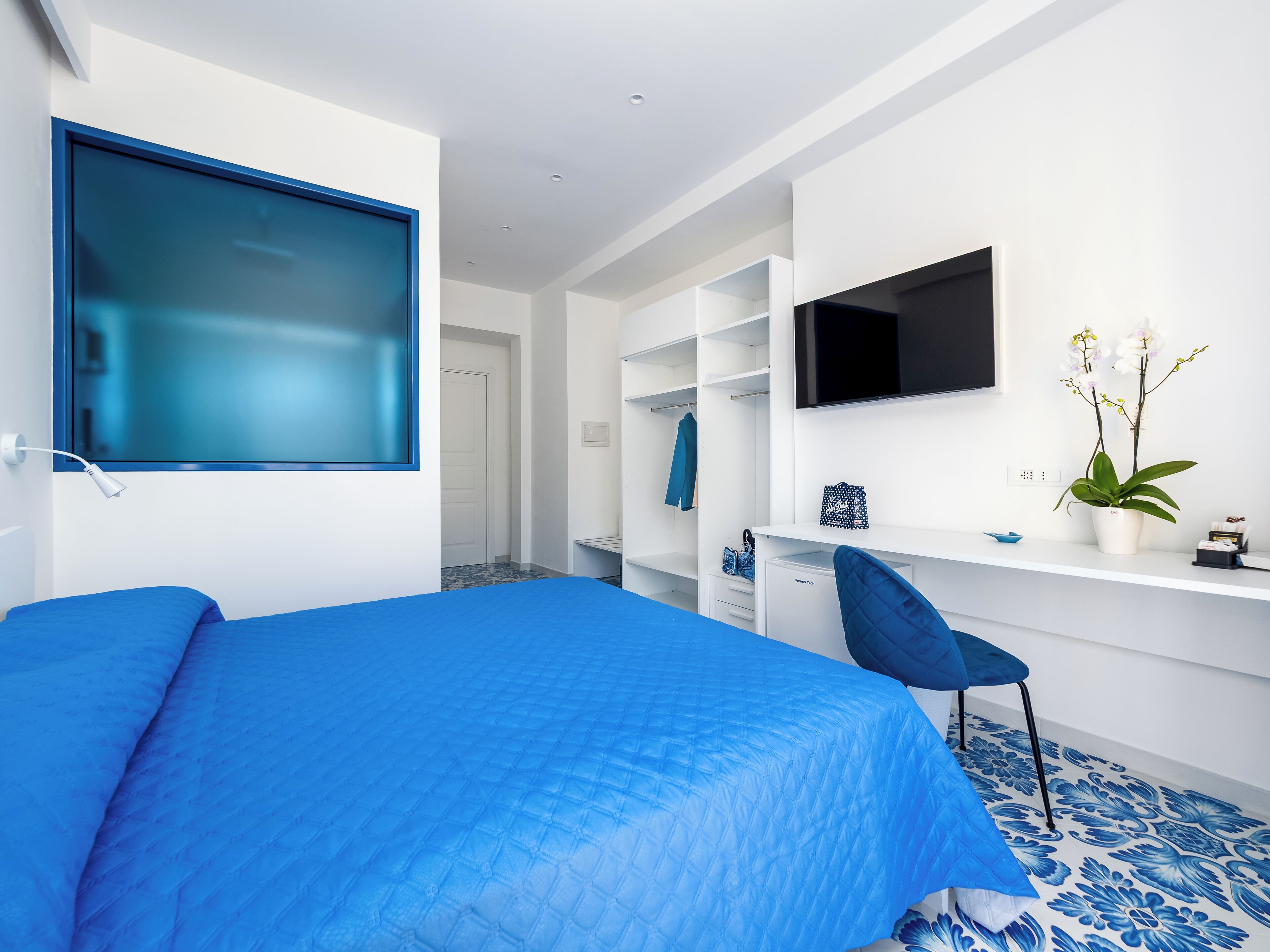 Ein modernes Schlafzimmer mit einem großen Bett, einem Schreibtisch, einem Stuhl und einem an der Wand befestigten Fernseher.