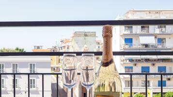Ein Tisch mit einer Prosecco-Flasche und zwei Gläsern auf einem Balkon mit Blick auf eine Stadtlandschaft.