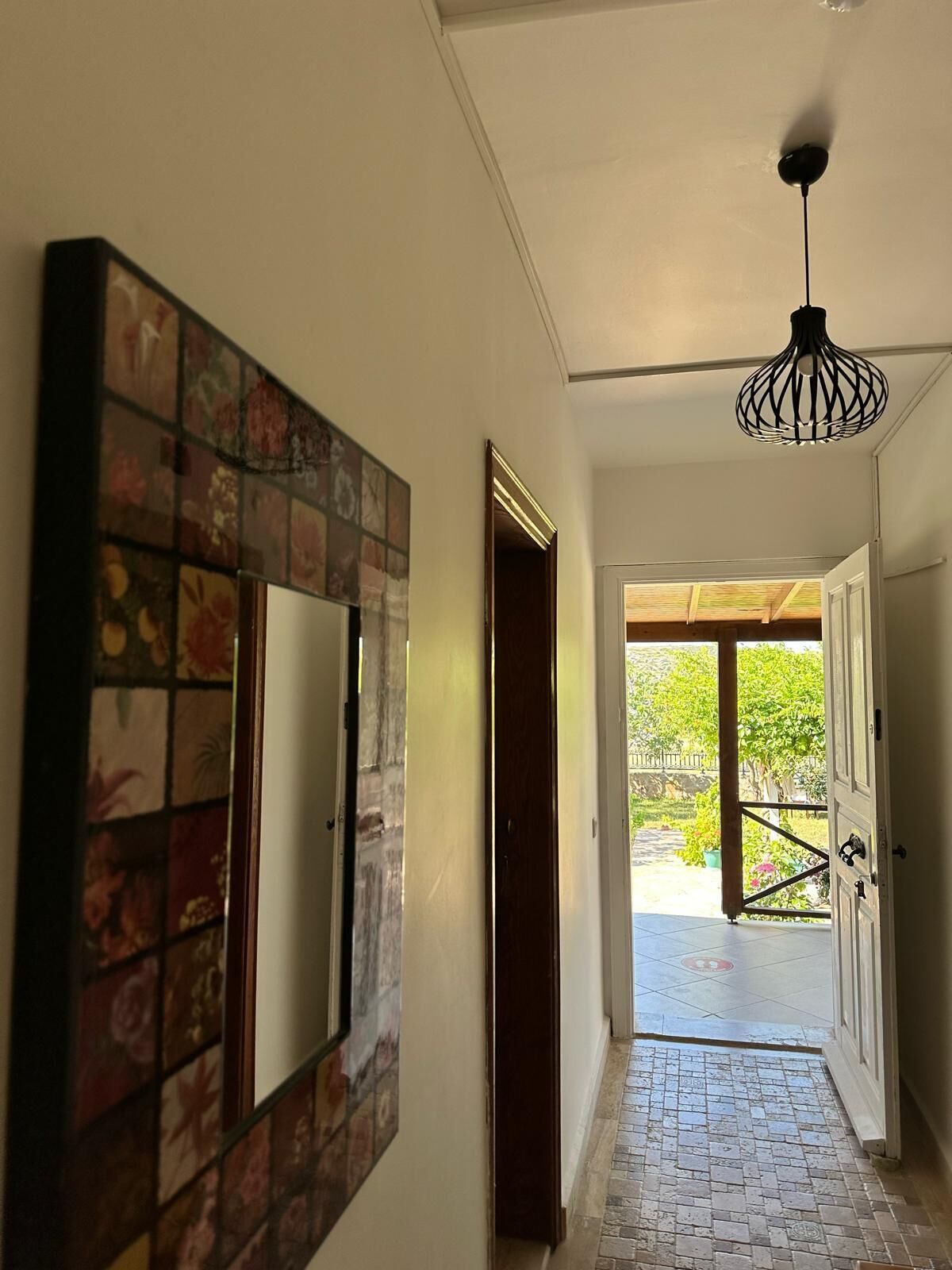 A hallway with a tiled floor, a wall-mounted mirror, and a ceiling light fixture.