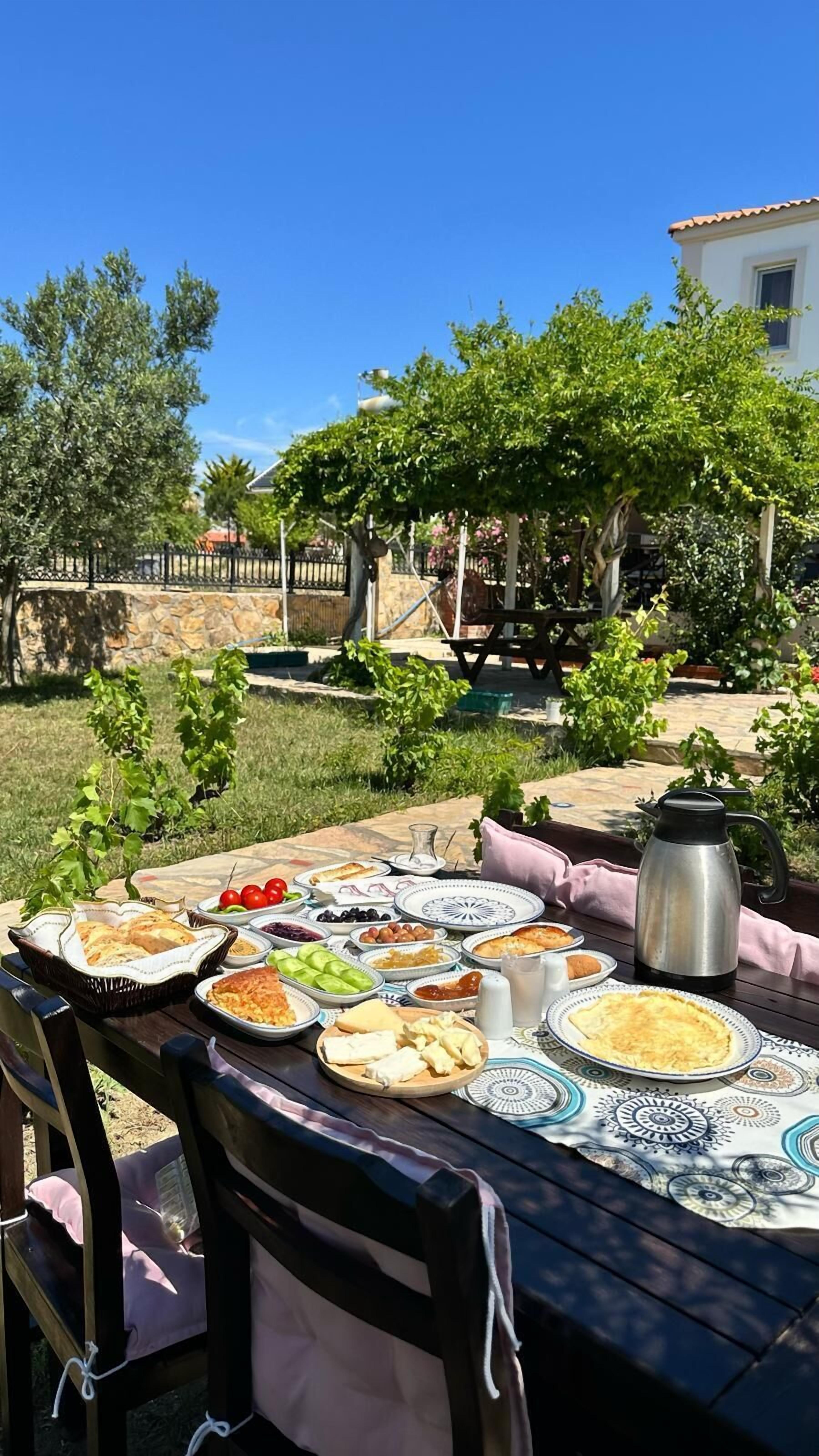 An outdoor dining area with a table set for a meal, surrounded by greenery and a stone wall.