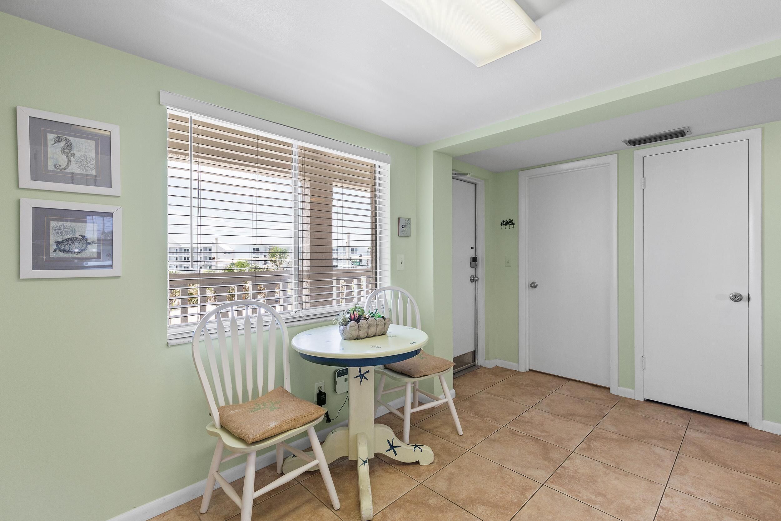 A room with a round table, two chairs, a window with blinds, and a door.