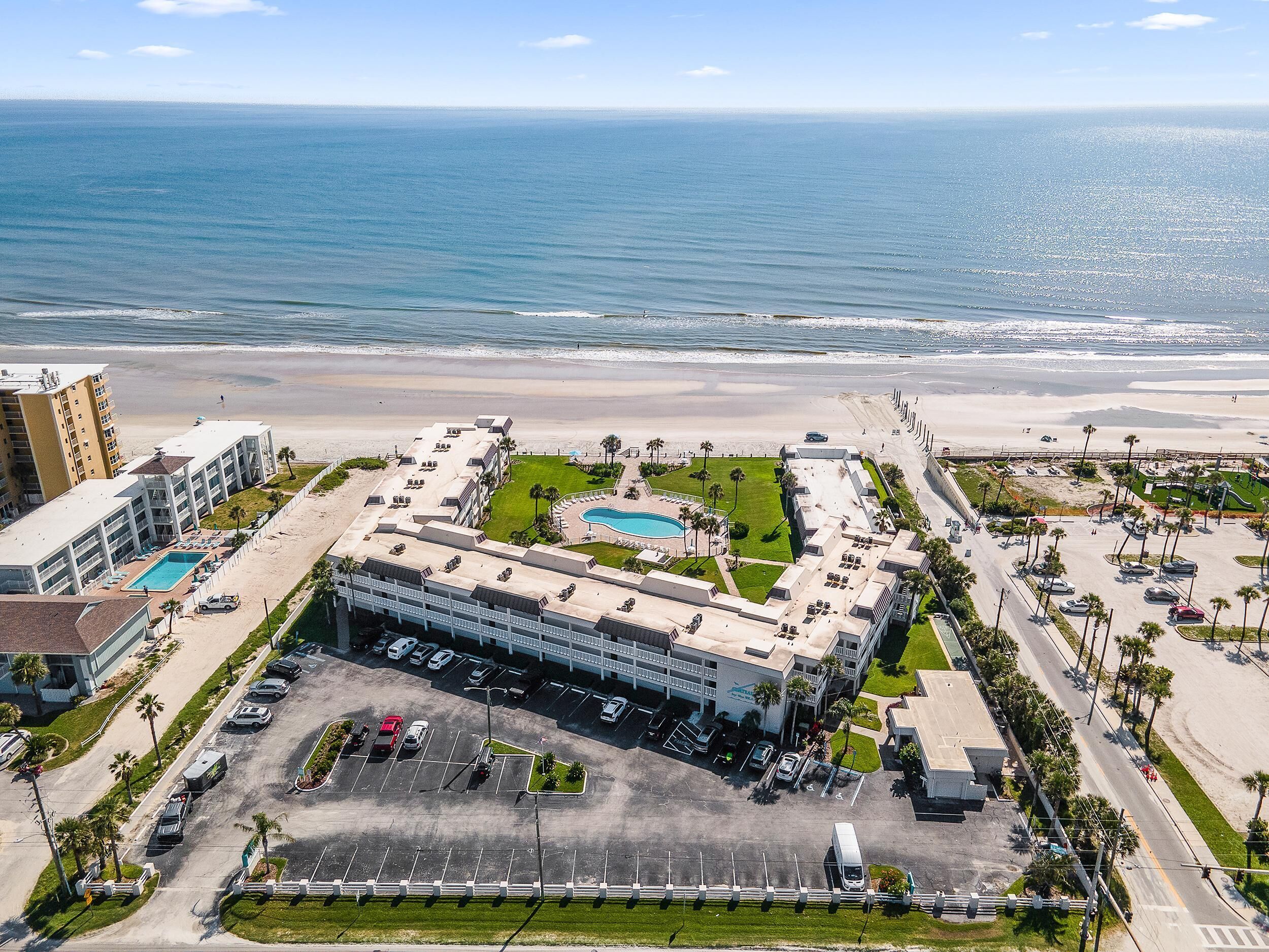 An aerial view of a hotel with a pool, parking lot, and beachfront access.