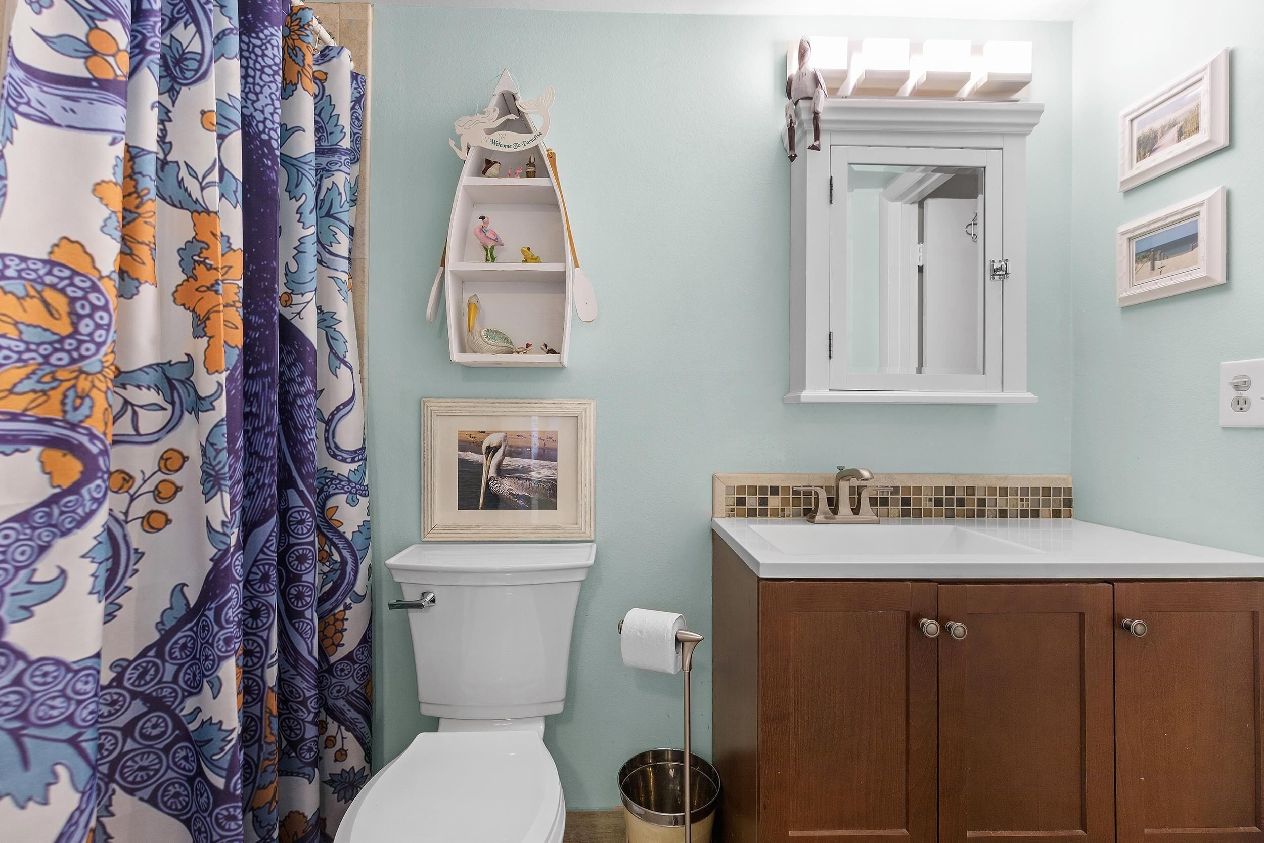 A bathroom with a toilet, a sink, a cabinet, a decorative shelf, and a shower curtain.
