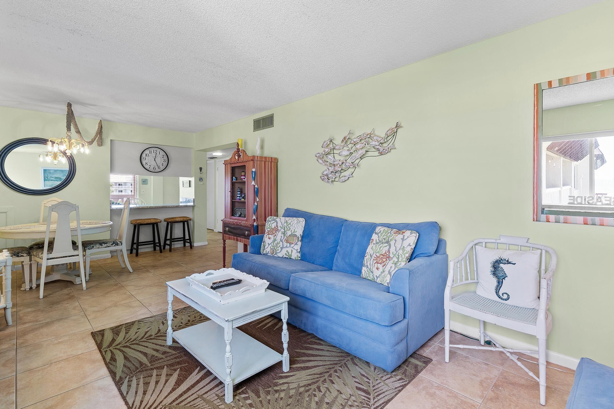 A living room with a blue sofa, white armchair, and a dining area with a table and chairs.