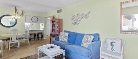 A living room with a blue sofa, white armchair, and a dining area with a table and chairs.