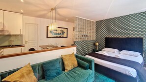 A modern hotel room with a green sofa, a bed with a dark headboard, a dining area with a white table, and a patterned wall. - N&J - REFLET D'OR - Vieux Nice - Neau beach (Niza)