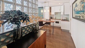 A modern kitchen with white cabinets, a dining area with a wooden table and chairs, and a large window with a decorative plant. - N&J - REFLET D'OR - Vieux Nice - Neau beach (Niza)