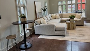 Een ruime woonkamer met een grote hoekbank, een ronde salontafel en een eettafel met krukken.