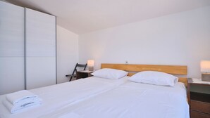 A neatly made bed with white linens and pillows, a wooden headboard, and a nightstand with a lamp. - Apartment Meri #2 by Litto (Basinci)