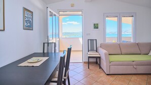 A room with a dining table, chairs, a sofa, and a view of the sea through large windows. - Apartment Meri #2 by Litto (Basinci)