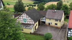 Un bâtiment traditionnel à colombages, doté d’une cour intérieure et entouré de verdure et de champs.
