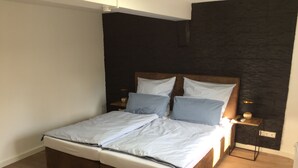 Une chambre moderne avec un lit en bois, une literie blanche et un mur d’accent de couleur foncée.