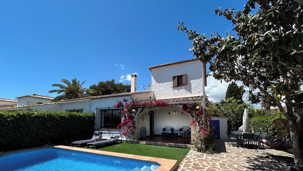 A swimming pool with a stone deck, a patio with outdoor furniture, and a white building with a tiled roof. - El Rincón del Montgó - private swimming pool (Xàbia)