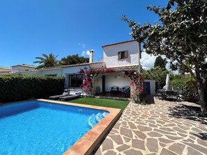 A swimming pool with a stone deck, a patio with outdoor furniture, and a white building with a tiled roof. - El Rincón del Montgó - private swimming pool (Xàbia)