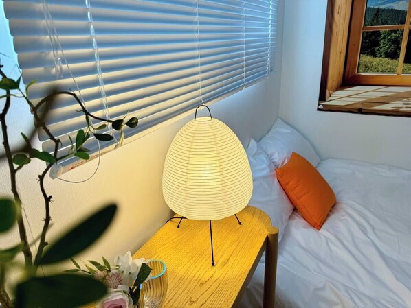 Et soveværelse med en seng, et sengebord med en lampe og et vindue med persienner.