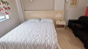 A bedroom with a bed, bedside table, lamp, and a wall with a picture. - Dingding Hotel (Shanghai Pudong Airport Heqing Town) (Shanghai)