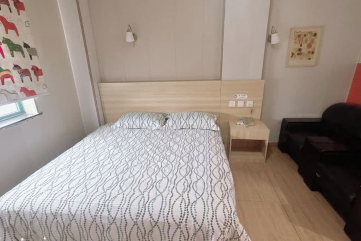 A bedroom with a bed, bedside table, lamp, and a wall with a picture.