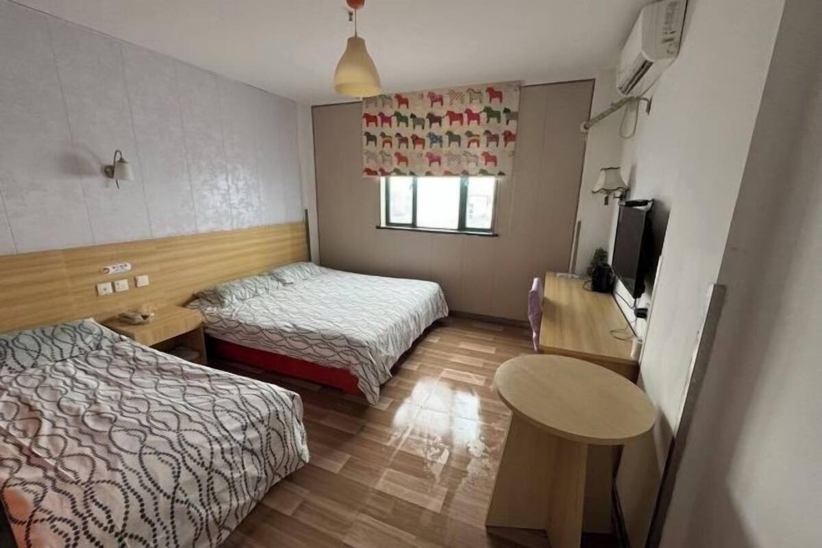 Ett hotellrum med två sängar, ett litet runt bord, en tv och ett fönster med en mönstrad gardin.